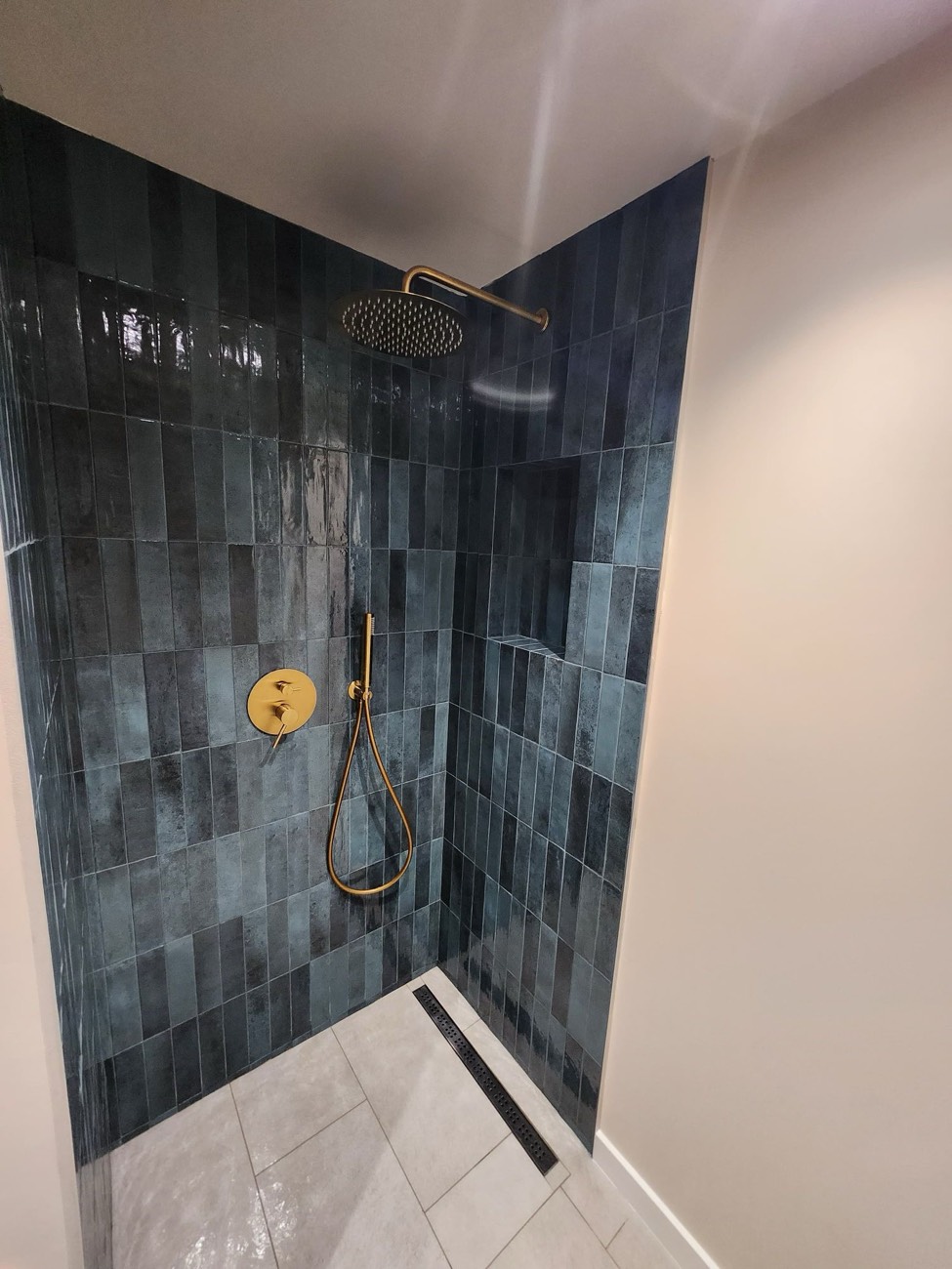 Walk-in shower in blue tile with brushed brass fittings and a linear drain