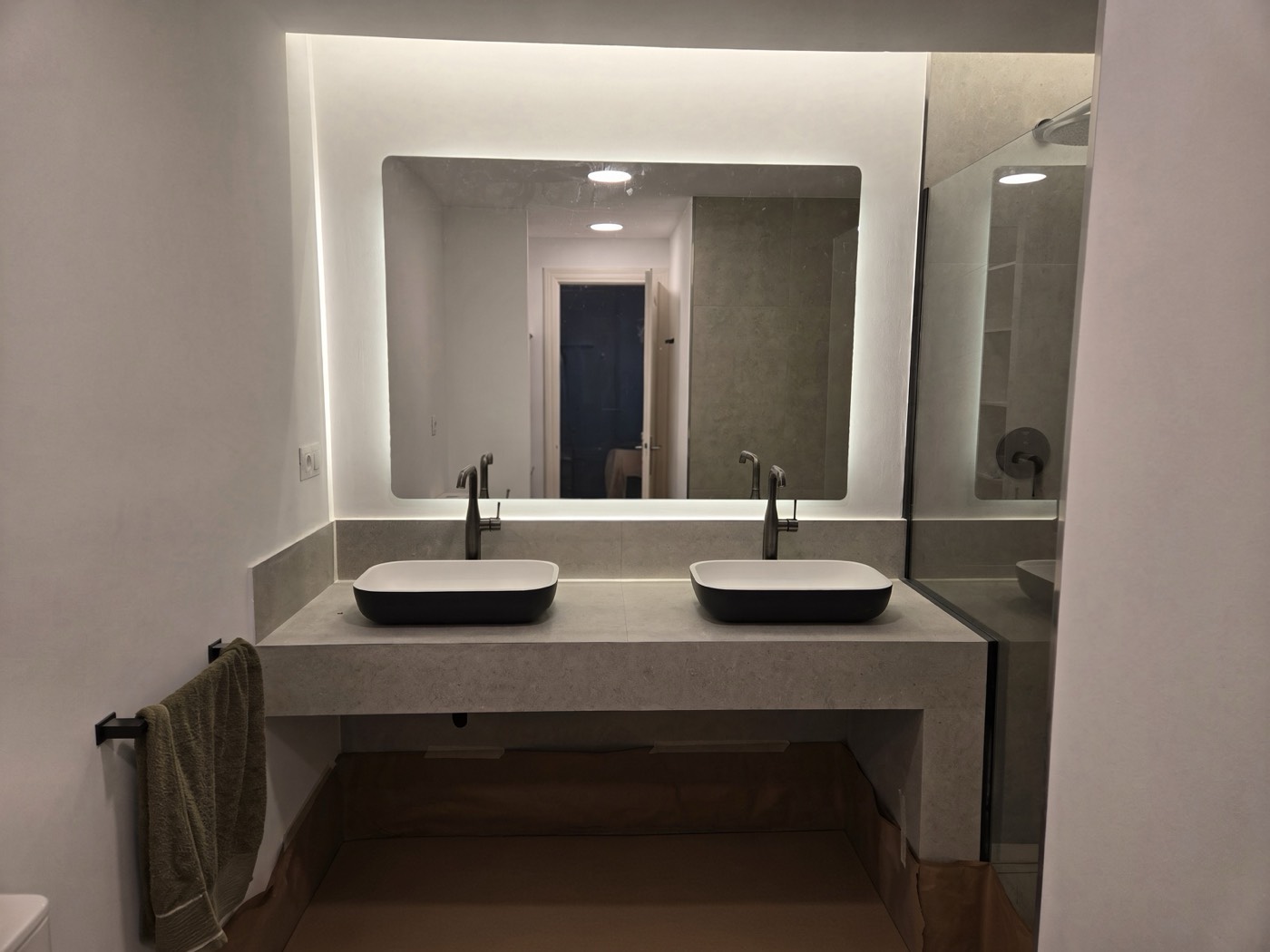 Twin basins on a poured vanity under a backlit mirror